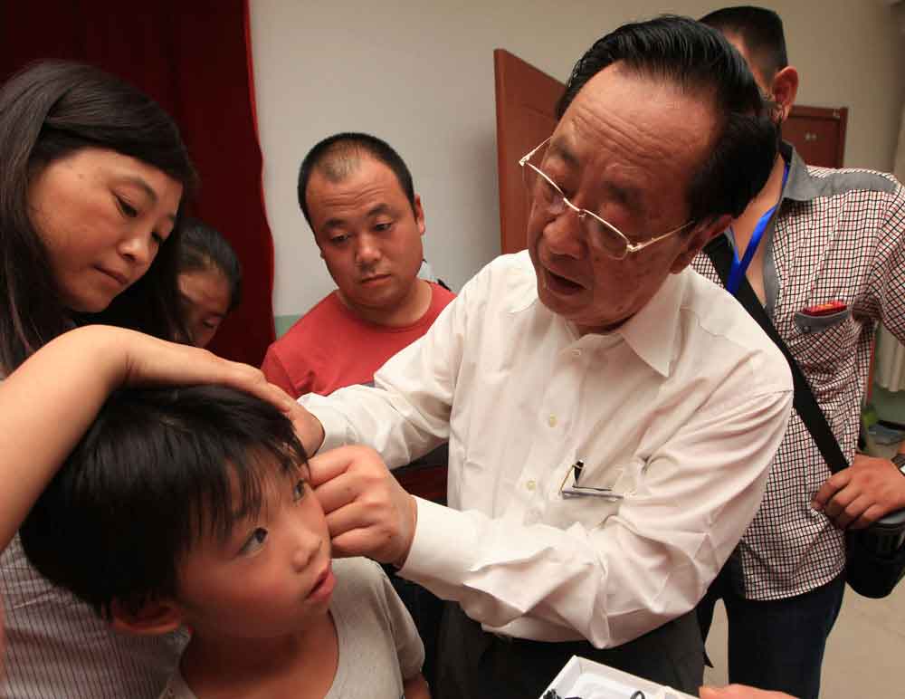 魏基成先生现场为聋哑儿童佩戴助听器，3天下来共帮助了600名儿童。